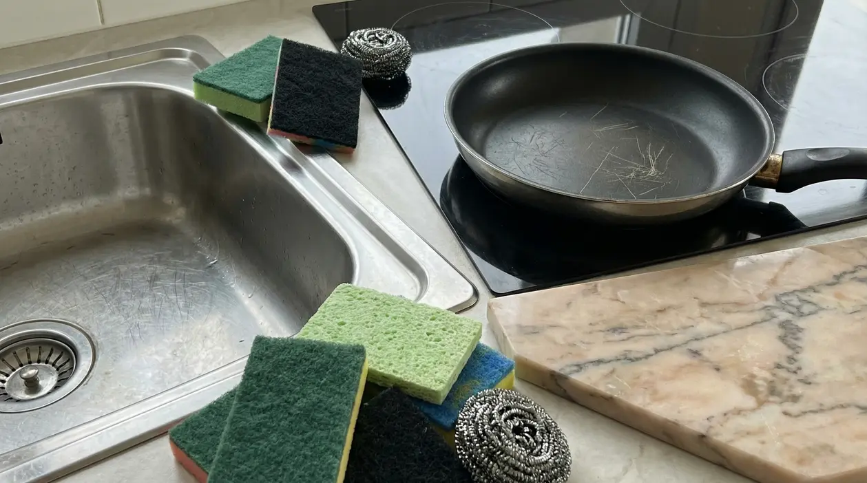 Spugne abrasive e pagliette metalliche vicino a lavello e padella graffiata
